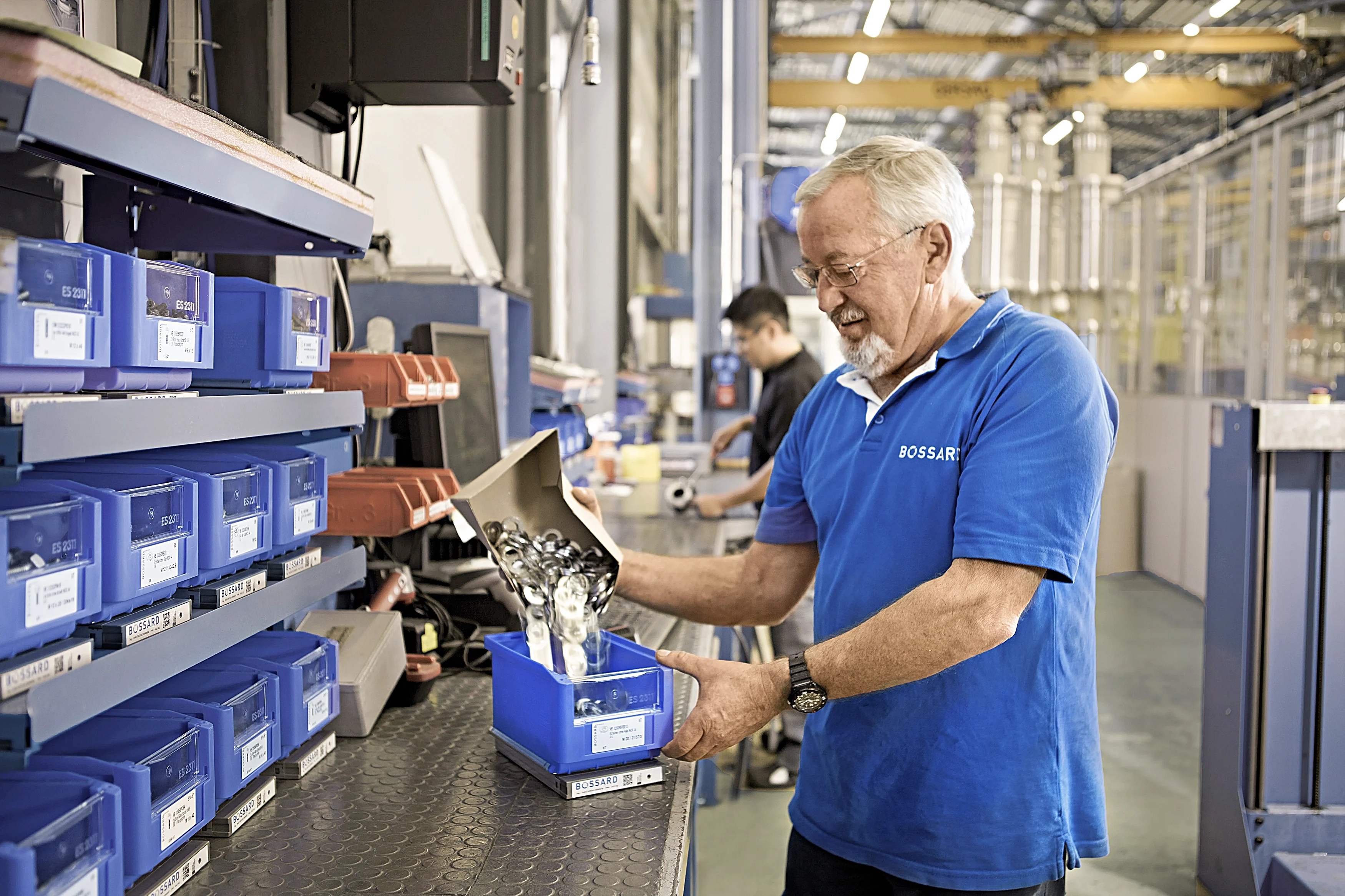 Bossard employee in blue shirt refilling SmartBin container at stock location.