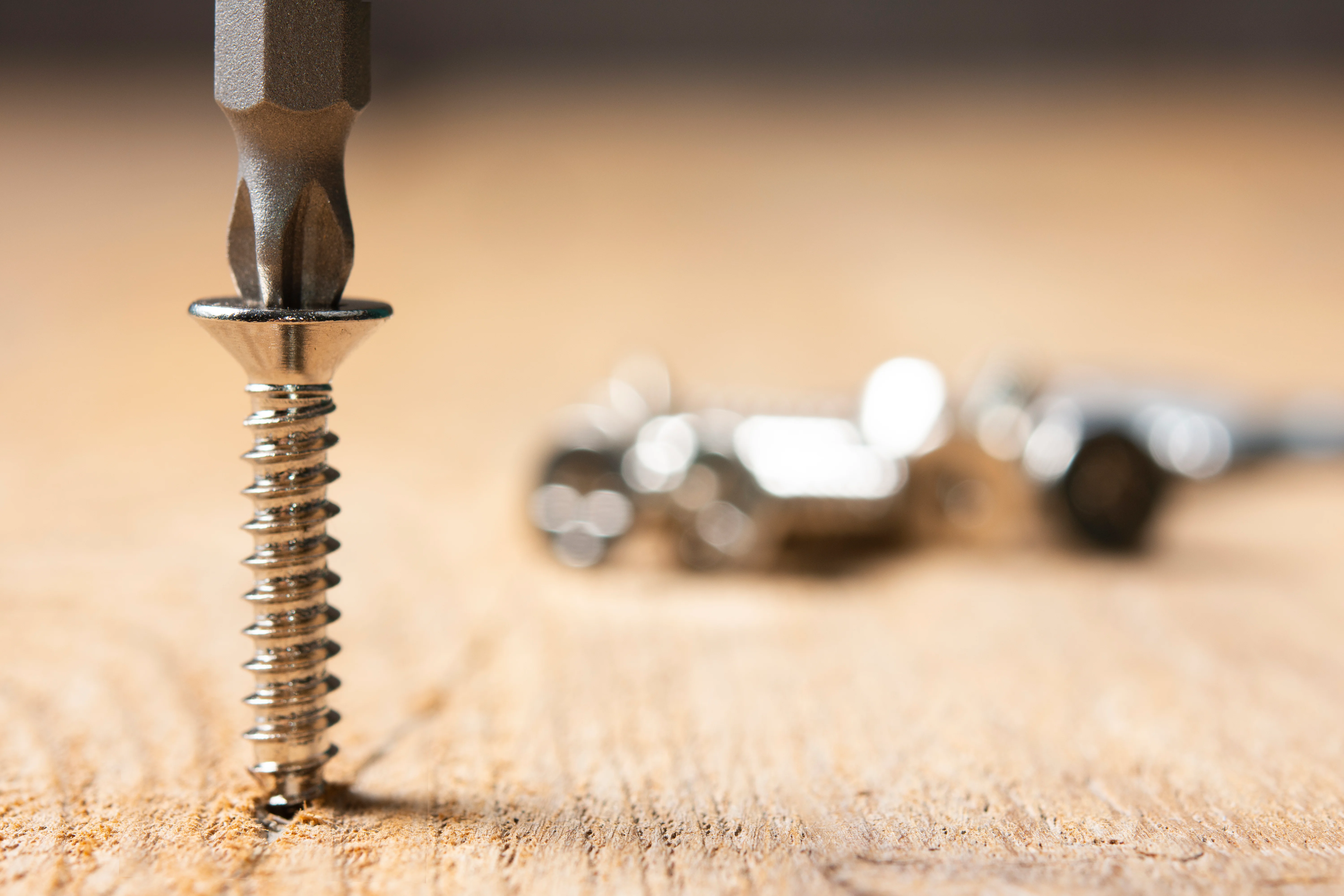 Close-up of a screw being drilled into a wood board with several other screws in the background